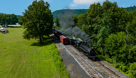 An Aerial View of a Narrow Gauge Steam Passenger Train, Approaching Traveling Thru Countryside, Blowing Smoke, on a Sunny Summer Day