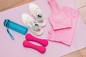 Two pink dumbbells, sportswear, sneakers, bottle of water on a yoga mat. Sport equipment for athlete