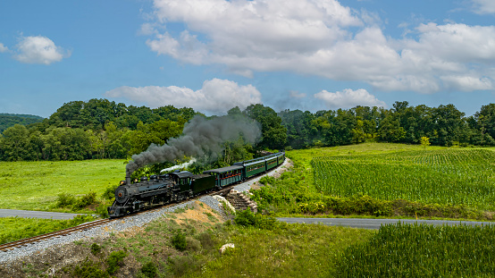 An Aerial View of a Narrow Gauge Steam Passenger Train, Approaching Traveling Thru Countryside, Blowing Smoke, on a Sunny Summer Day