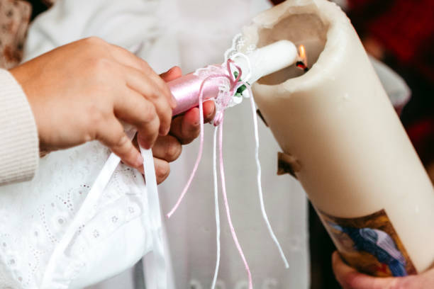 Godmother lighting a candle in the flame of a larger candle during a baptism ceremony A woman lighting a candle in the flame of a larger candle during a baptism ceremony according to the Catholic rite. pics of the godmother stock pictures, royalty-free photos & images