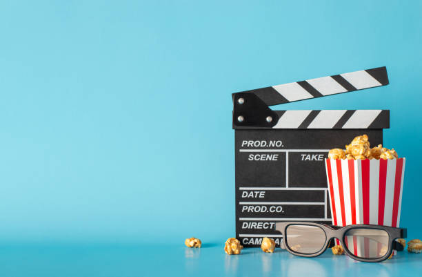 istock Experience excitement of much-awaited movie debut. Side view captures table scene with clapperboard, striped popcorn box, and 3D glasses against light blue wall, leaving space for text or film adverts 1865103675