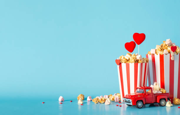istock Create a memorable cinematic Valentine's with food delivery. Side view table accents include tiny car model, striped popcorn boxes, heart decor, sprinkles. Light blue wall backdrop sets perfect scene 1865103684