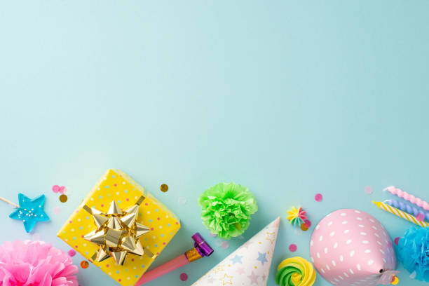 istock Dynamic anniversary celebration theme. Top-view decorated table with festive props, lollipops, present, birthday hats, noisemaker, candles, confetti, flowers on pastel blue background, space for text 1865103688