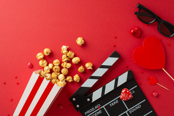 istock Cinematic Love Symphony: Overhead composition featuring slate, 3D glasses, spilled popcorn, candies, and heart-themed decor on vibrant red canvasâ charming setup for Saint Valentine's Day movie debut 1865104223