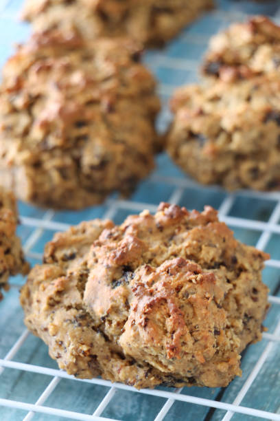 istock Full frame image of white cooling rack over blue, greaseproof parchment paper lined baking tray of freshly, cooked, homemade, rock cakes, rows of rustic sweet, dry fruit cakes, focus on foreground, home baking concept 1865110237