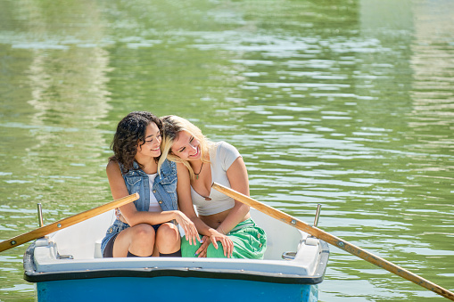 young lesbian couple smiling leaning on each other's shoulders in a rowboat on a pond