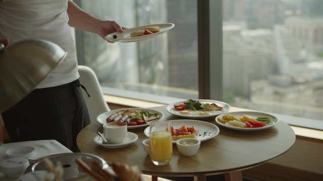 A man in a hotel on a skyscraper places breakfast plates on the table