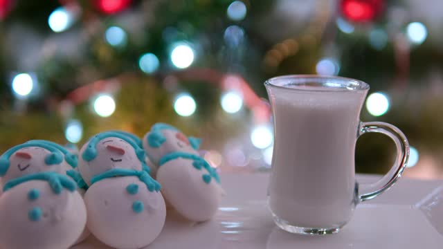 a glass of hot milk near the Christmas tree meringue snowmen on a white plate delicious Snack dinner spending time celebrating Christmas Healthy food color light bulbs