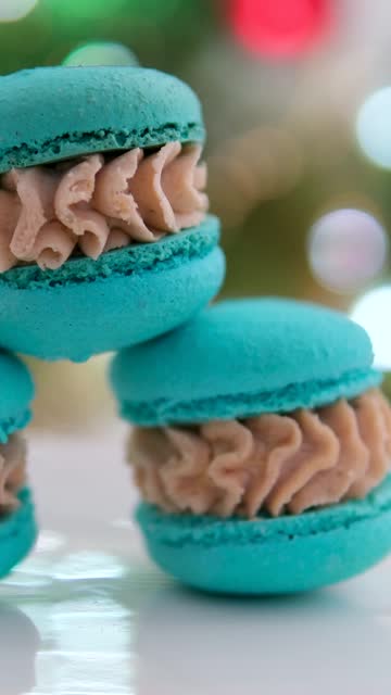 against the background of a Christmas tree on a plate dessert macaroons red blue green pink and orange French pastries made from almond flour with cream delicious appetizing yami yami