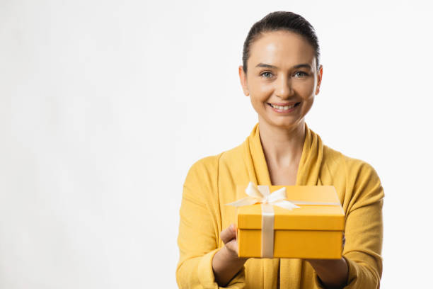 A Woman Is Holding Gift Box Smiling woman holding a yellow gift box. dişiler stock pictures, royalty-free photos & images