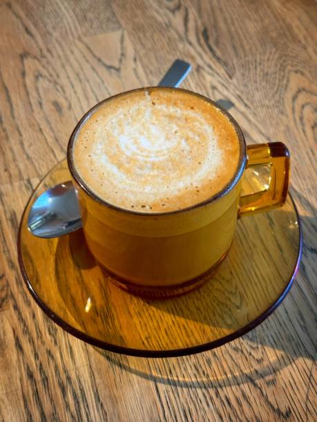 Flat white coffee in orange mug on wood grain table stock photo