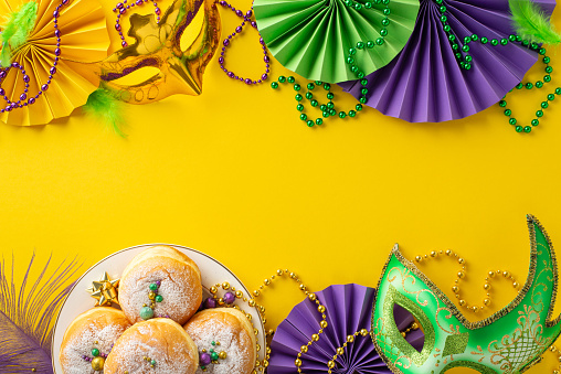 Party Spectacle composition: Top view photo showcasing energetic table arrangement with carnival masks, delicious donuts, fans and more all set on vivid yellow surface, offering space for text or ad