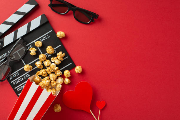 istock Film of Love: top view shot featuring clapperboard, 3D glasses, popcorn spilled from box, and heart-themed decor on a passionate red backdropâan ideal setting for a romantic movie premiere 1865157607