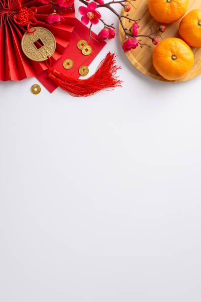 istock Celebrate Chinese New Year's vibrancy through this top view vertical composition showcasing fan, Hong Bao, lucky coin charm wall hanging, tangerines on white neutral background with sakura accents 1865158011