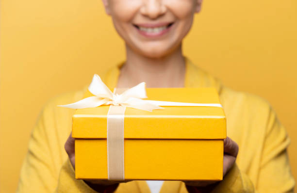 Woman Holding Gift Box Smiling woman holding a yellow gift box. dişiler stock pictures, royalty-free photos & images