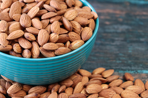 Stock photo showing close-up view of some shelled almonds that are piled high in a turquoise dish, against a blue woodgrain background. Raw almonds are considered to be a very healthy snack food, containing vitamin E, antioxidants and protein, and boasting a list of health benefits while aiding blood sugar control.