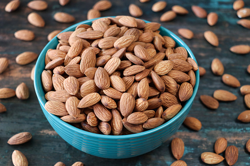 Stock photo showing close-up view of some shelled almonds that are piled high in a turquoise dish, against a blue woodgrain background. Raw almonds are considered to be a very healthy snack food, containing vitamin E, antioxidants and protein, and boasting a list of health benefits while aiding blood sugar control.