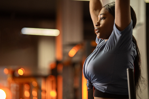 Close-up shot of beautiful African woman hangs on the wall bars and raises her legs in the gym