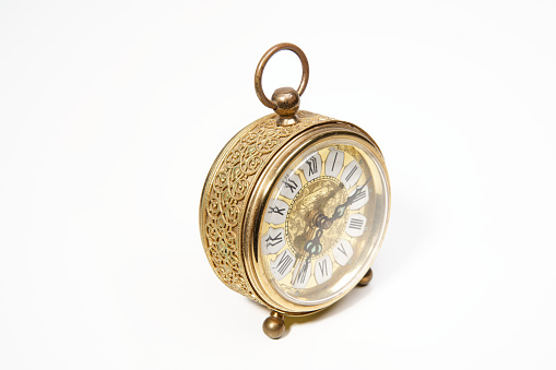 an old golden analog alarm clock with mechanical movement isolated on a white background