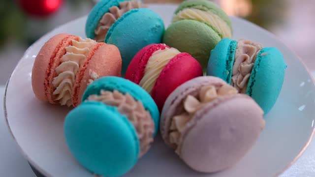 against the background of a Christmas tree on a plate dessert macaroons red blue green pink and orange French pastries made from almond flour with cream delicious appetizing yami yami