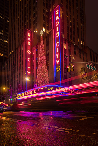 Radio City Music Hall marquee in the rain, traffic whizzes by in a blur. December 17, 2023. New York City, NY. USA