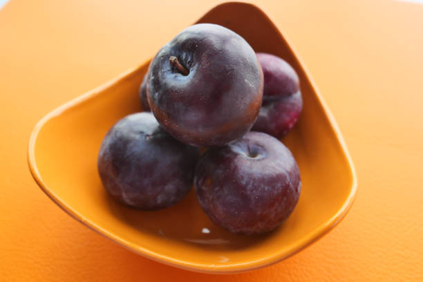 Fresh plums in a bowl on orange color background