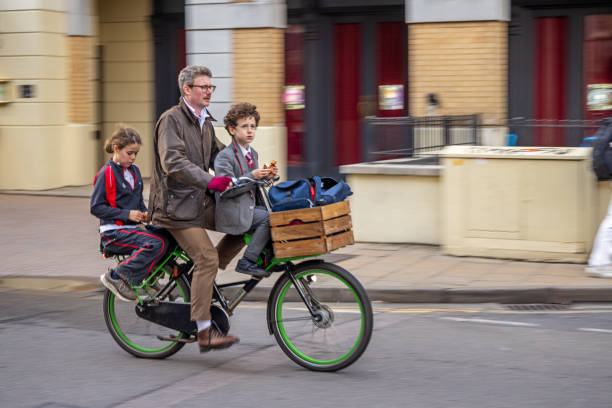 Downing Street, Cambridge, England - November 9th 2023:  Father driving two kids home from school on a bicycle