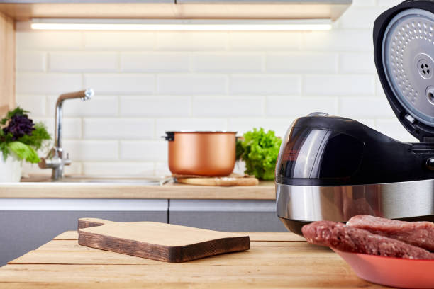 istock Domestic electric multi cooker and uncooked ingredient on kitchen table. Wooden board with vegetables and meat. 1865283037