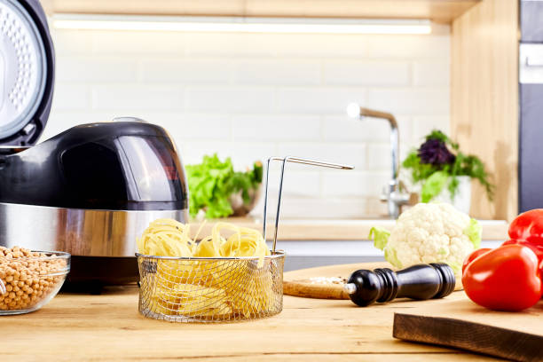 istock Multi cooker and spaghetti pasta on wooden table in kitchen. Cooking spaghetti or raw nest noodles in a pot. Homemade uncooked ribbon fettuccine. Dry long rolled macaroni close up. 1865283040