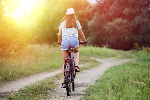 Young happy woman in a casual wear rides a bicycle in a summer meadow. Beautiful girl enjoys summer nature. Relax, rest, nature concept.