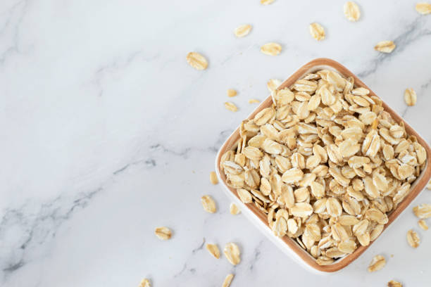 Rolled oats (raw oatmeal flakes) in bowl isolated on white marble background. Top view, copy space.