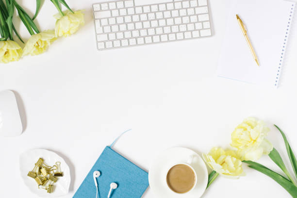 istock Office workspace with a white desk. Top view from above with a keyboard, notepad, flowers and pencil with a white cup of coffee on a plate. Flat surface with copy space. Women's business concept 1865305220