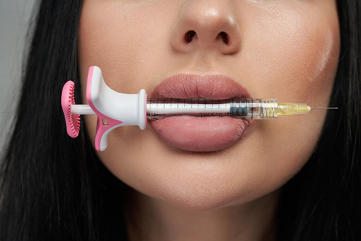Attractive woman's face keeping syringe between lips.