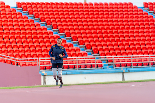 Wide shot and front view of sport man athlete prosthesis legs is jogging on track in the stadium to practice before copetition in the big event.