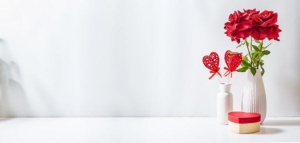 Red roses in a vase on a white table. Mock up for displaying works.Valentine's day holiday background concept