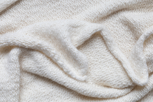 Wool fabric texture close-up background. Knitted warm beige, white sweater or scarf with folds. Top view, flat lay