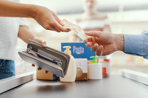 Cash payment at the supermarket: woman buying groceries and giving cash money to the cashier, hands close up
