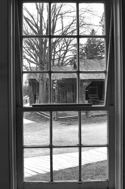 Black and white image of a rustic view through a windowpane, showcasing bare trees and a countryside setting.