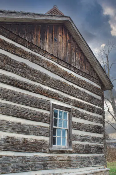 Rustic wooden cabin exterior with a single window, showcasing weathered logs and vintage architectural details against a cloudy sky.