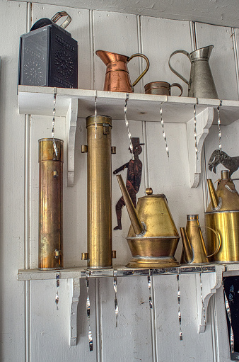 Vintage metal pitchers and containers on a wooden shelf against a white wall, with a rustic and antique look.
