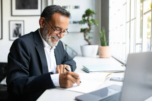 istock Cheerful mature european man in suit work on laptop, making notes, signing contract in modern office 1865408428