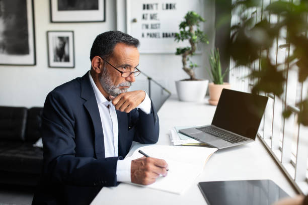 istock Pensive serious caucasian old businessman in suit with contract make notes, look at computer with empty screen 1865409002