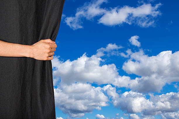 Hand opening black curtain with sky behind it