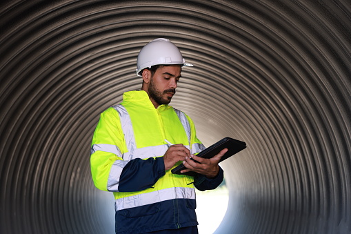 senior engineer holding a tablet  working on a huge pipe