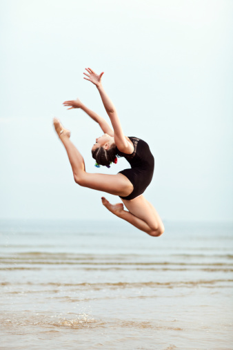 Young female gymnast jumping over sea surface.
