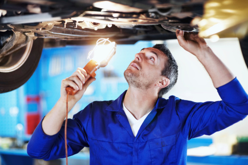 Automotive mechanic peering underneath a car while holding a lamp