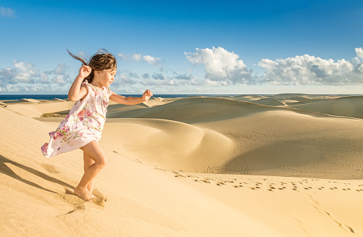 5 year old girl enjoying running in the beautiful sand dunes along the seaside of Maspalomas, Gran Canaria (Spain)