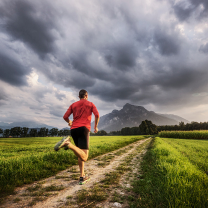 Muscular young man running toward the mountains at sunset as clouds approach.