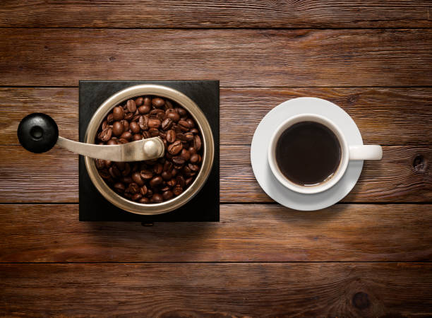 inquadratura dall'alto di tazza di caffè e rettificatrici su sfondo in legno - coffee coffee bean coffee grinder cup foto e immagini stock