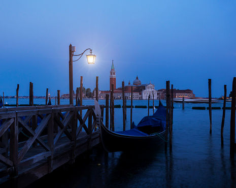 Lone lamp illuminates the pier, near which stands alone gondola.